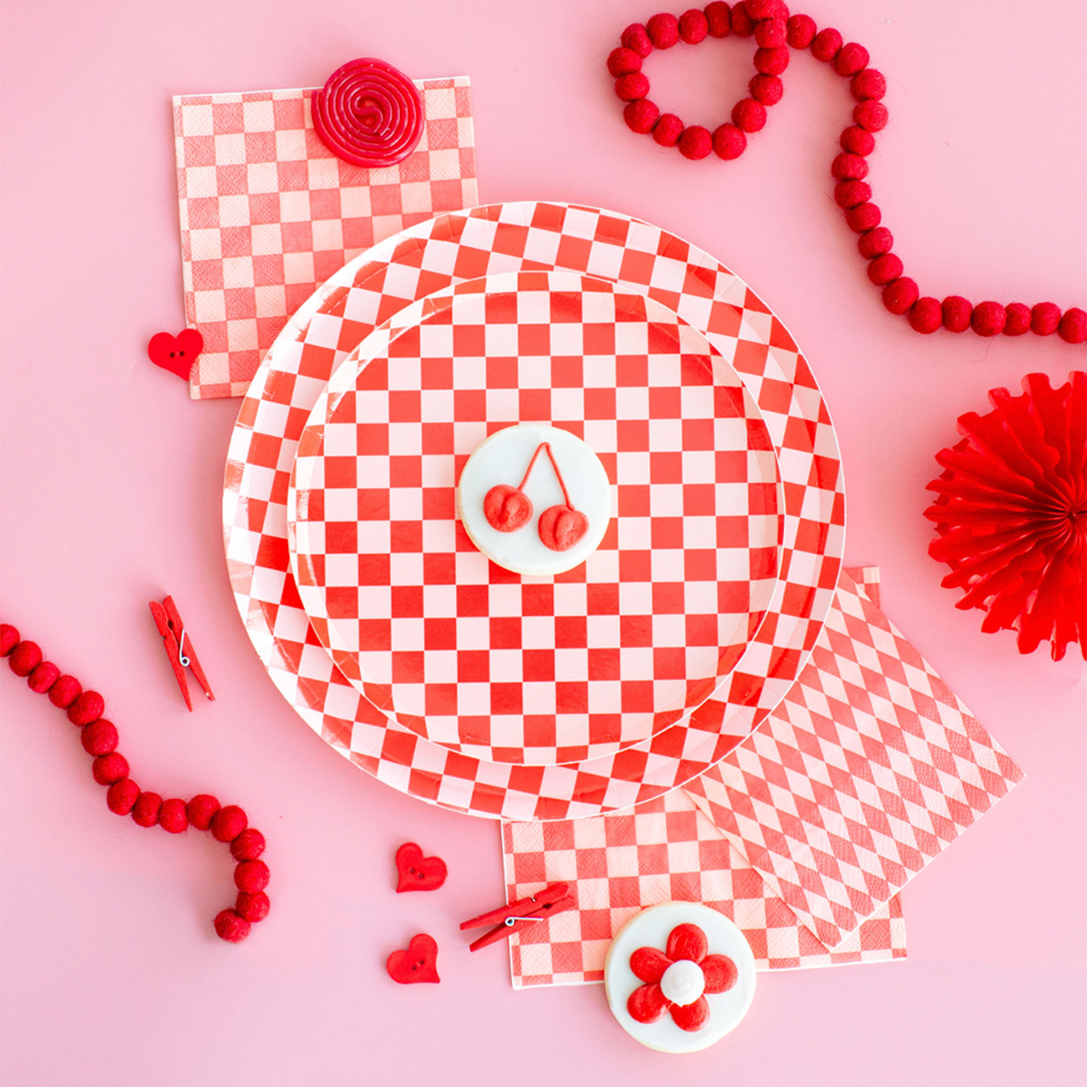 Red checkerboard dinner plates styled with matching napkins, cherry cookies, and red décor accents for a modern party table in Toronto.