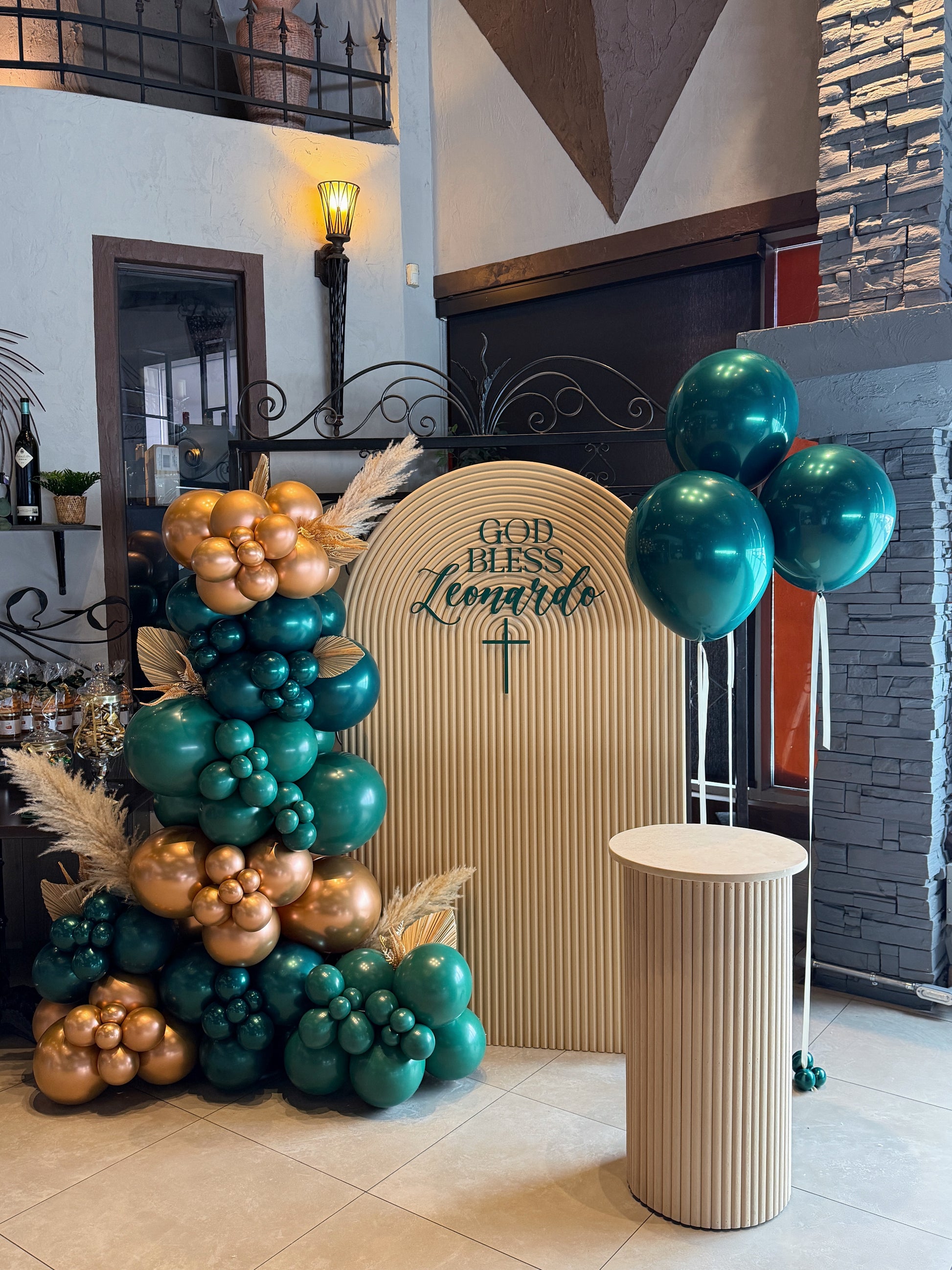 Sacrament event backdrop with emerald green and gold balloon garland and plinth display available at our Toronto party shop