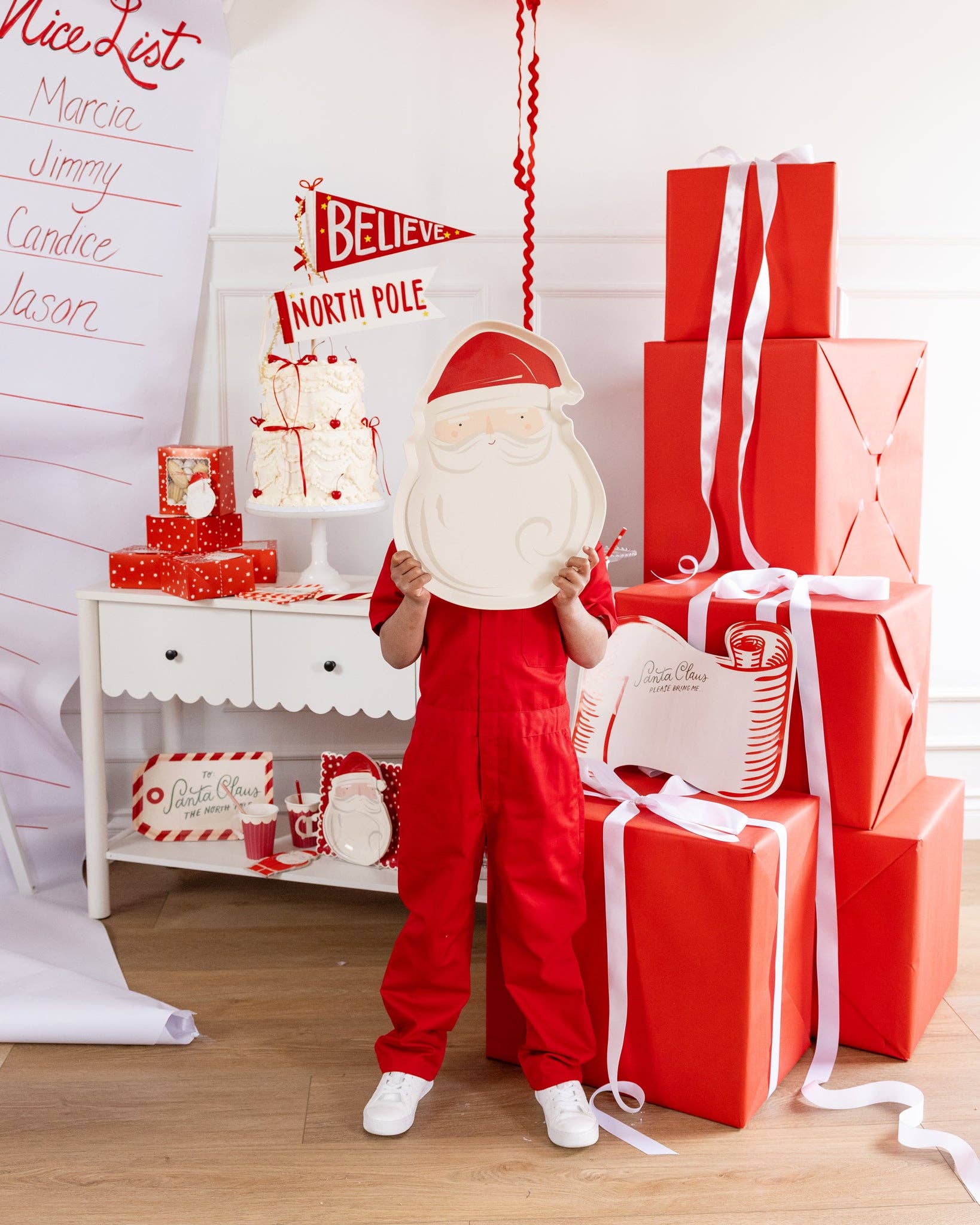 Child holding Santa bamboo tray beside red and white Christmas décor sold at Confetti My Party Toronto.