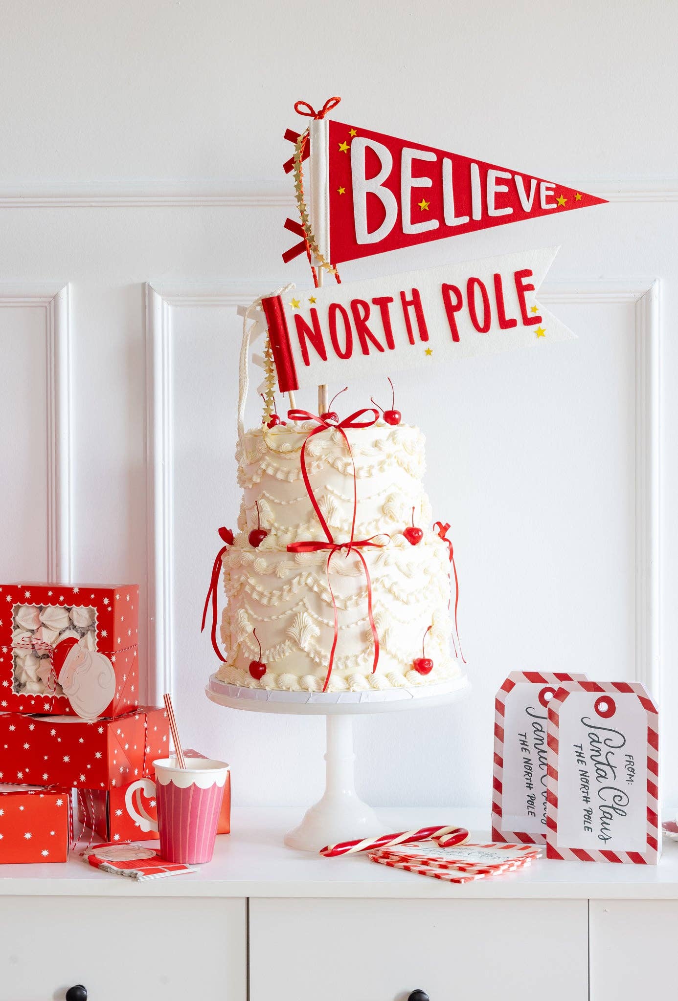 Christmas table display with Santa tag-shaped napkins, festive cake, and red holiday decorations. Sold at Confetti my Party in Toronto and ships Canada wide.