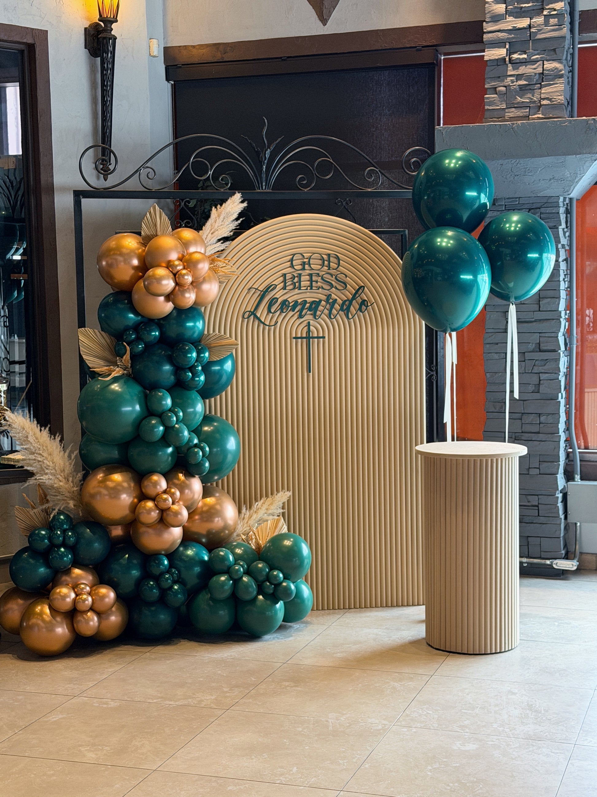 Arched sacrament backdrop with emerald green and gold balloon garland + plinth available in Toronto.