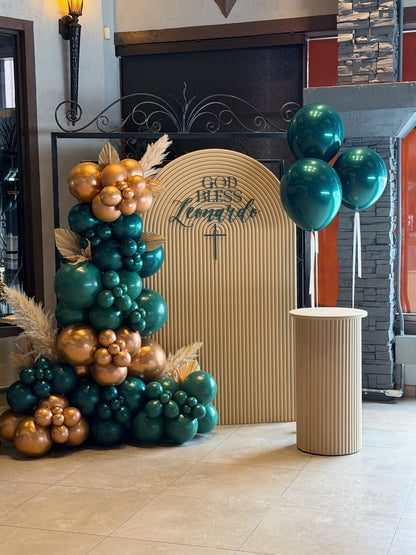Arched sacrament backdrop with emerald green and gold balloon garland + plinth available in Toronto.
