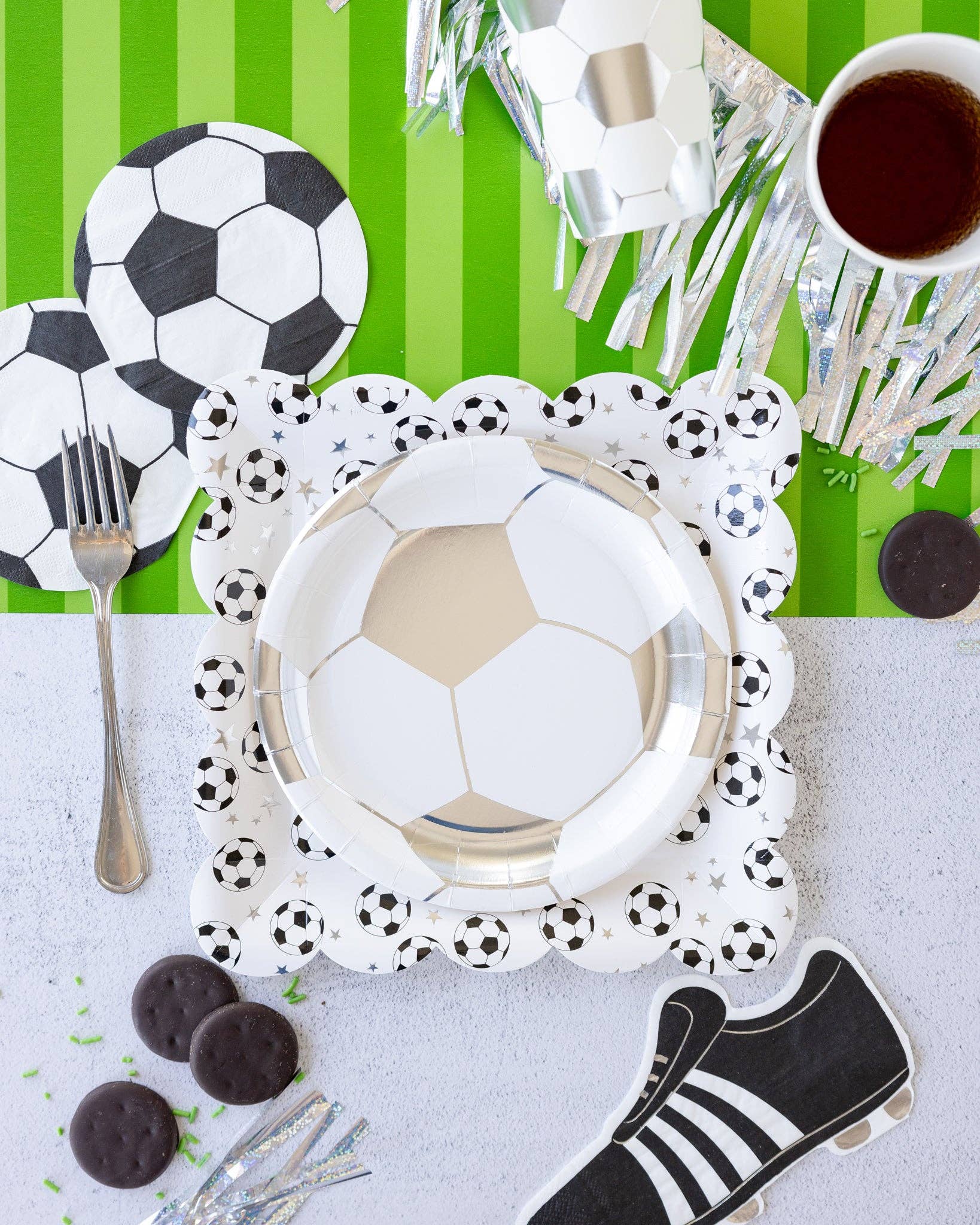 Soccer-themed table setting with plates, cutlery, and decorative items on a green and white striped background.
