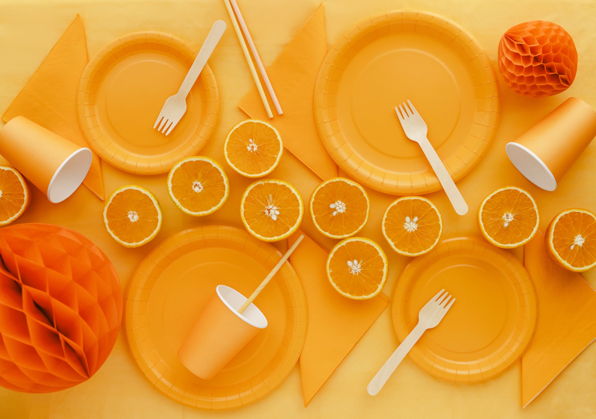 Orange-themed table setting with plates, cups, forks, and oranges on a yellow background.
