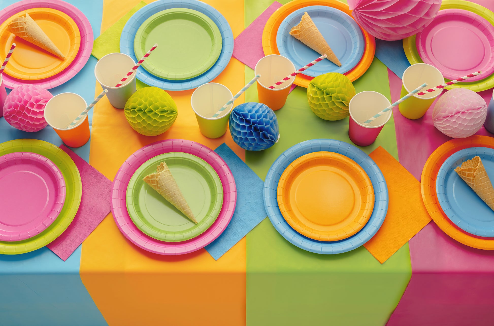 Colorful table setting with plates, cups, and ice cream cones on a multicolored surface.