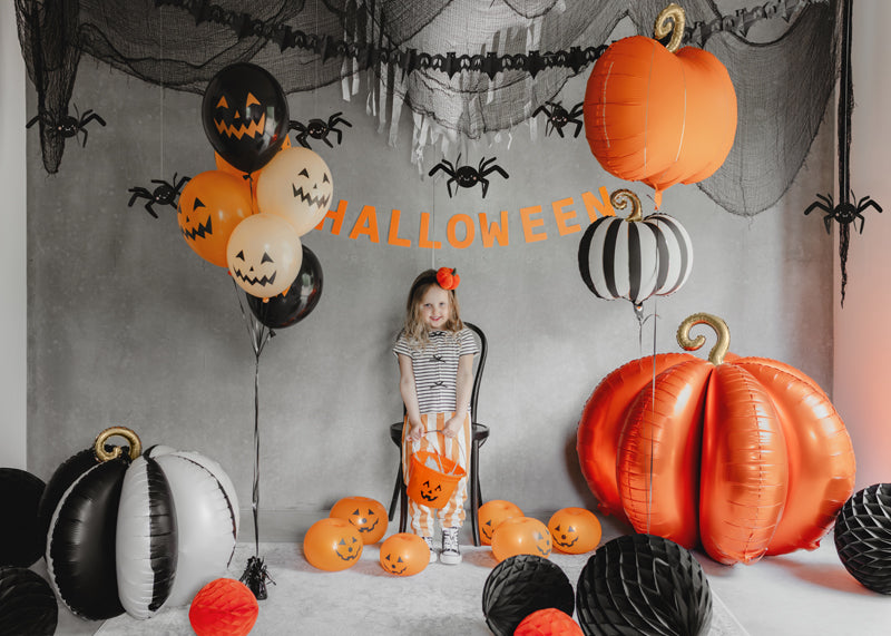 Halloween-themed room with balloons, pumpkins, and a child sitting on a chair.