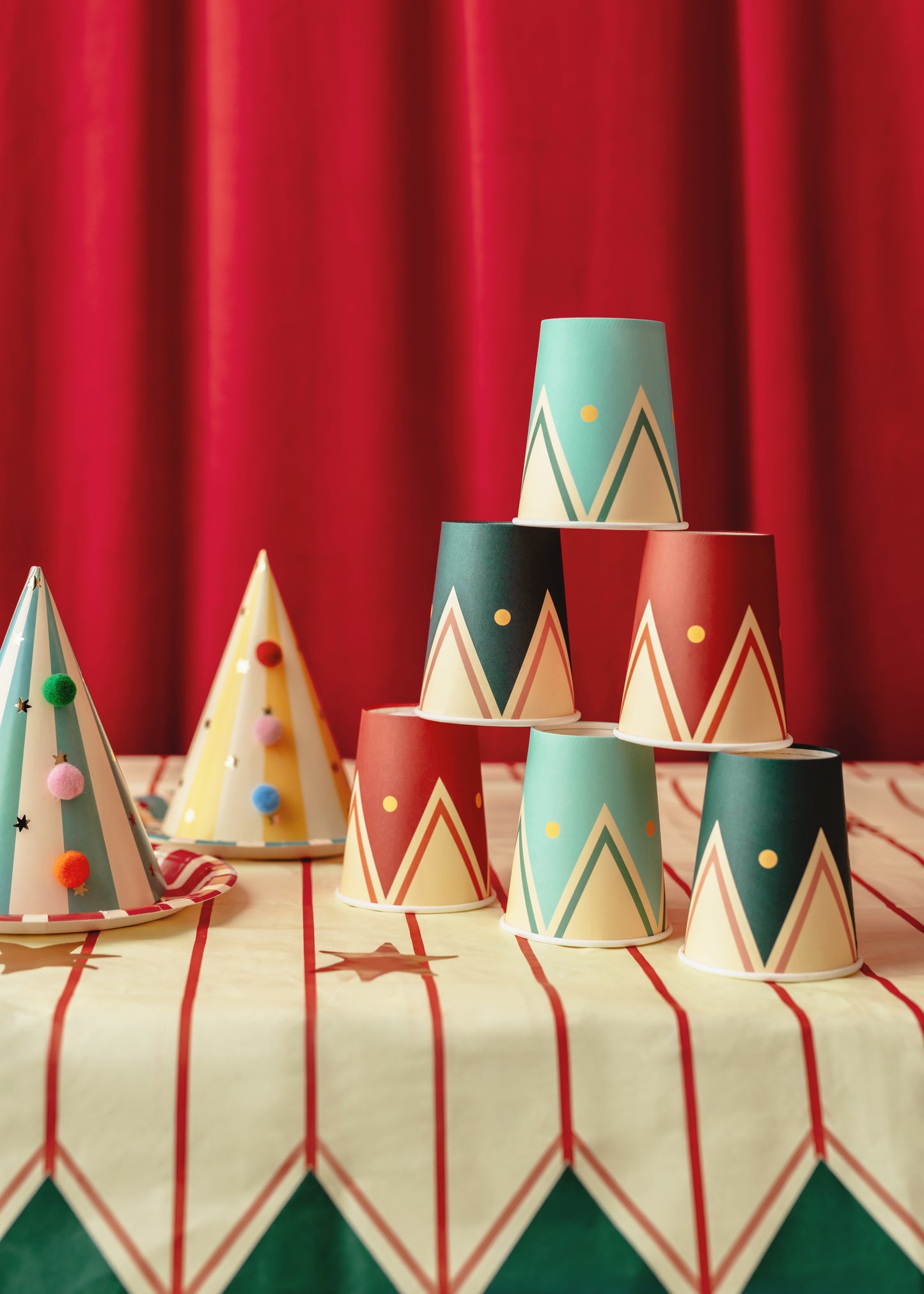circus themed paper table cover with matching pompom party hats and paper cups 