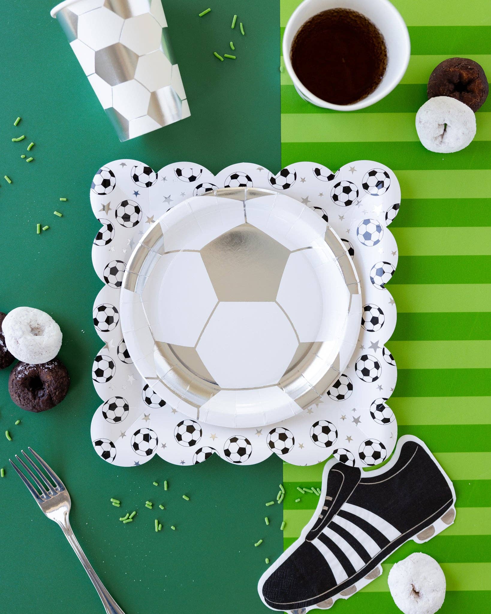 Soccer-themed party setup with paper plates, cup, and shoe on a green and white striped background.
