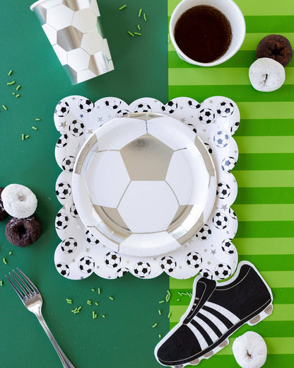 Soccer-themed party setup with paper plates, cup, and shoe on a green and white striped background.