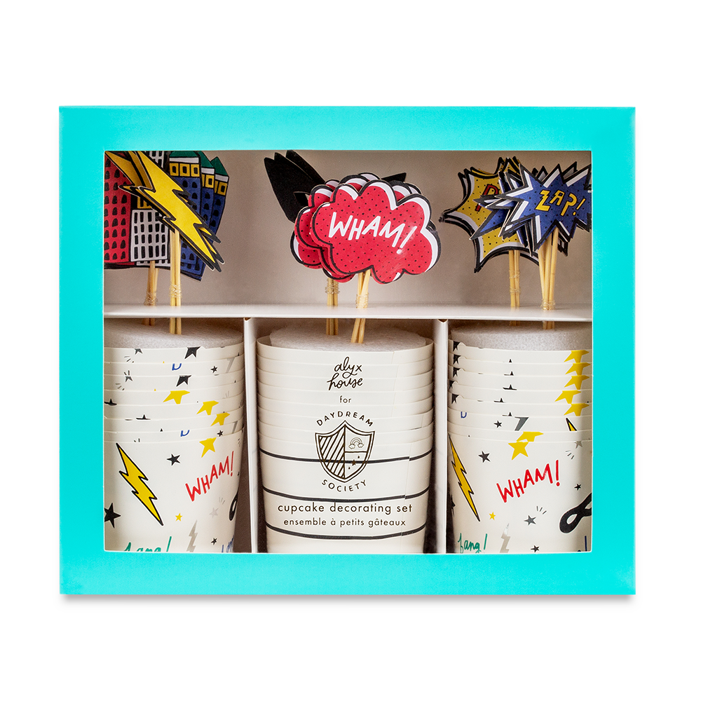 A boxed cupcake decoration set with three stacks of white paper cups printed with comic-style stars and lightning bolts, plus matching party toppers including a red 'WHAM!' cloud and yellow/blue comic burst pieces, all displayed in a turquoise box.