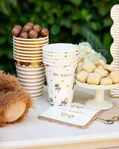 Neutral Oh Baby themed table setup with tan striped cups, gold napkins, and treats for Toronto celebrations.