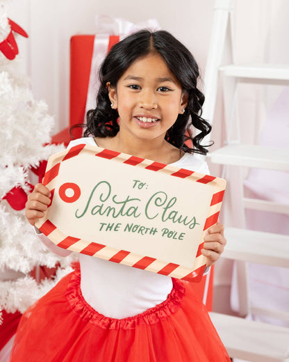 Little girl holding ‘To Santa Claus’ bamboo tray by white Christmas tree, Toronto holiday photo setup.
