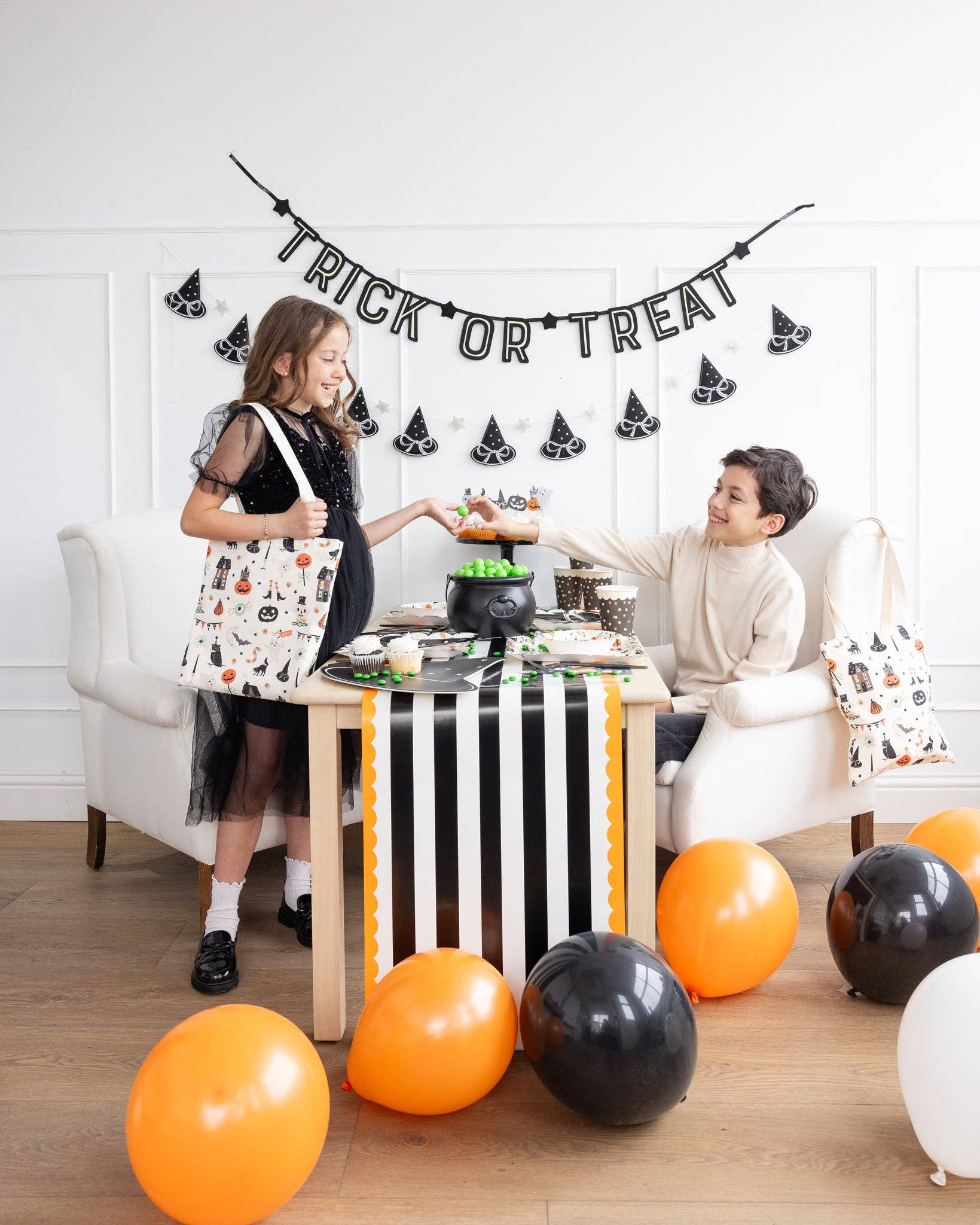 Two children at a Halloween-themed table with balloons and decorations.