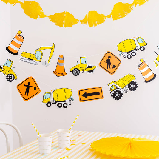 Under construction party banner with illustrated trucks, traffic cones, and roadwork signs styled above a party table, available at Confetti My Party in Toronto