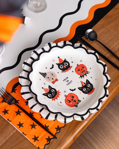 Halloween-themed plate with black cats, pumpkins, and ghosts on a wooden table.