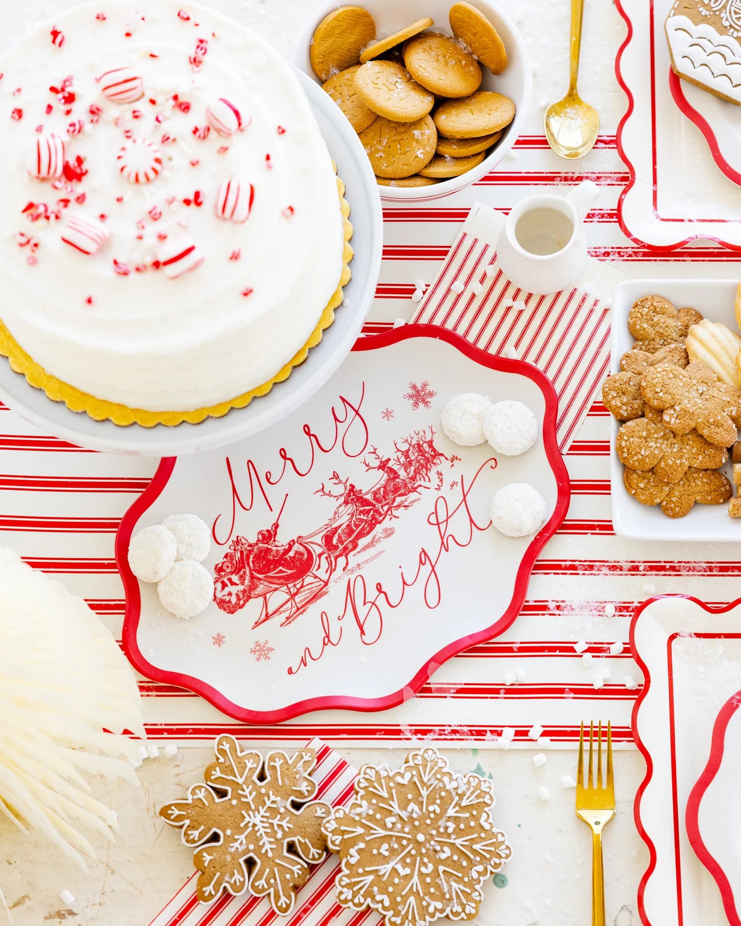 Christmas-themed table setting with cookies, cake, and decorative 'Merry and Bright tray on a red and white striped tablecloth.