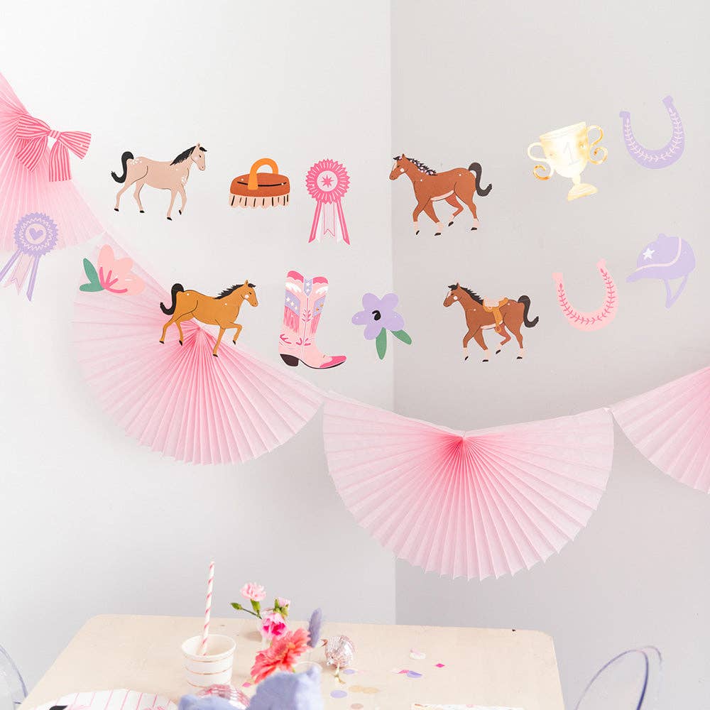 Decorative wall with horse-themed decorations including paper fans, ribbons, and cowboy hats on a light gray background.