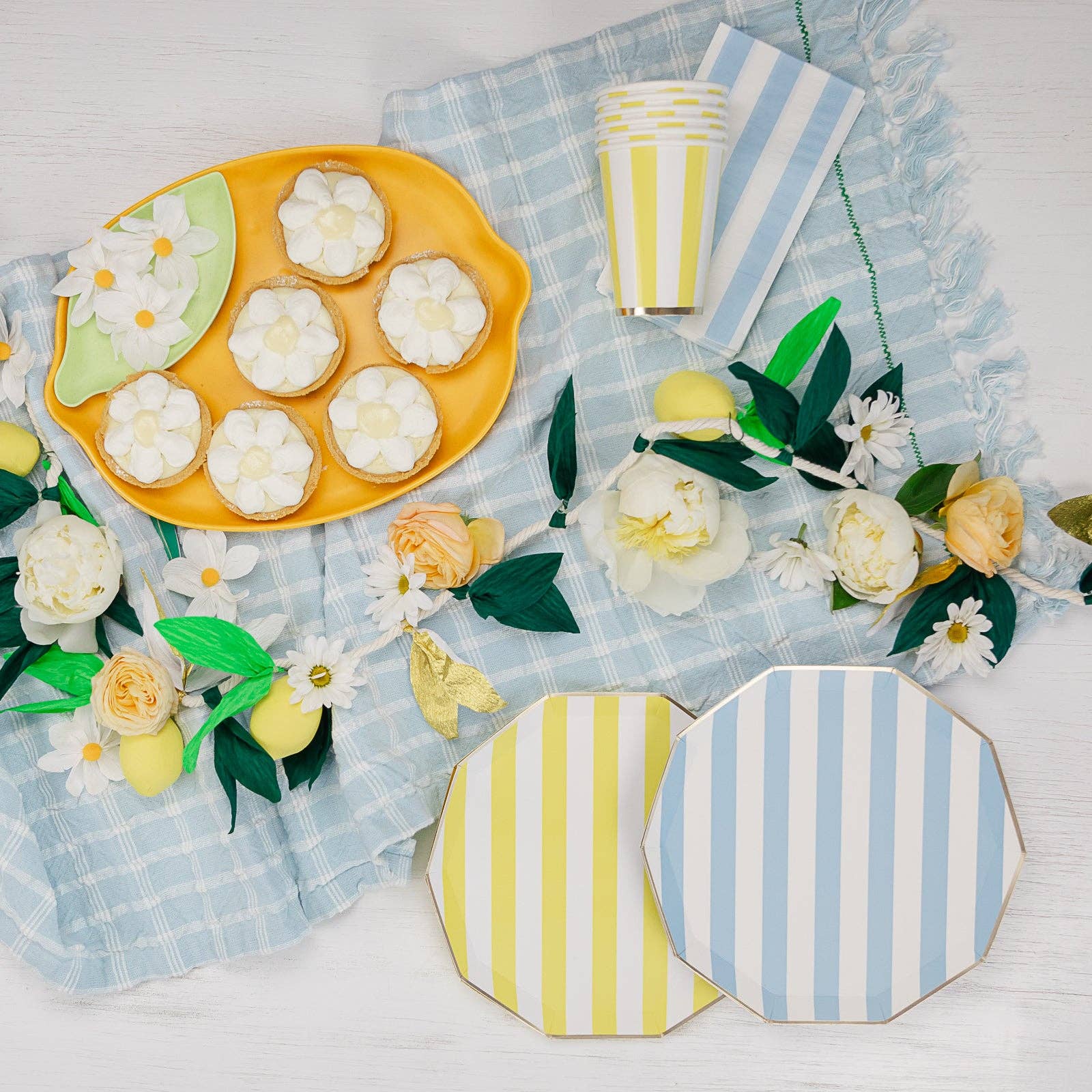 Decorative table setting with lemon-shaped cookies, striped cups, and floral decorations on a checkered cloth.