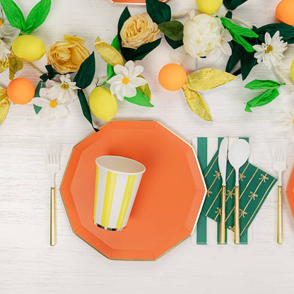 Colorful table setting with orange plates, yellow and white flowers, and green leaves on a white surface.