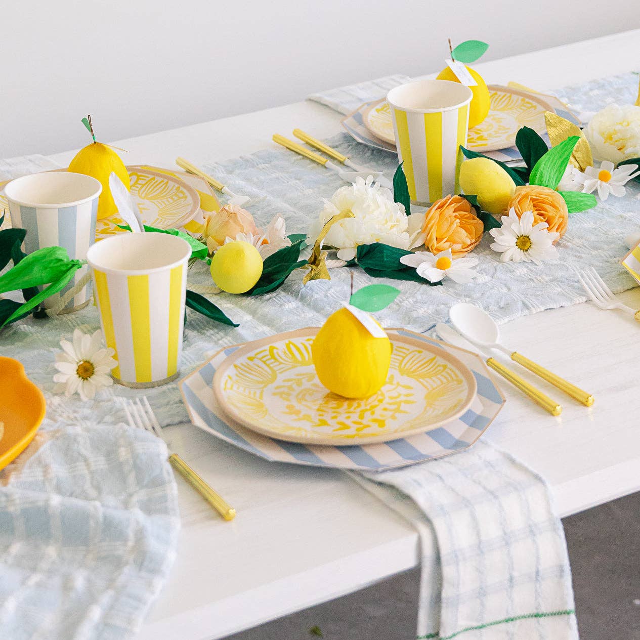Decorative table setting with yellow and white striped cups, plates, and lemons on a marble surface.
