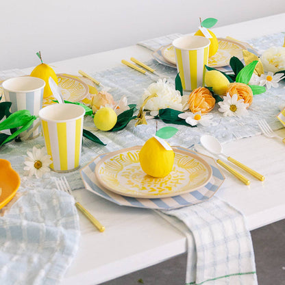 Decorative table setting with yellow and white striped cups, plates, and lemons on a marble surface.