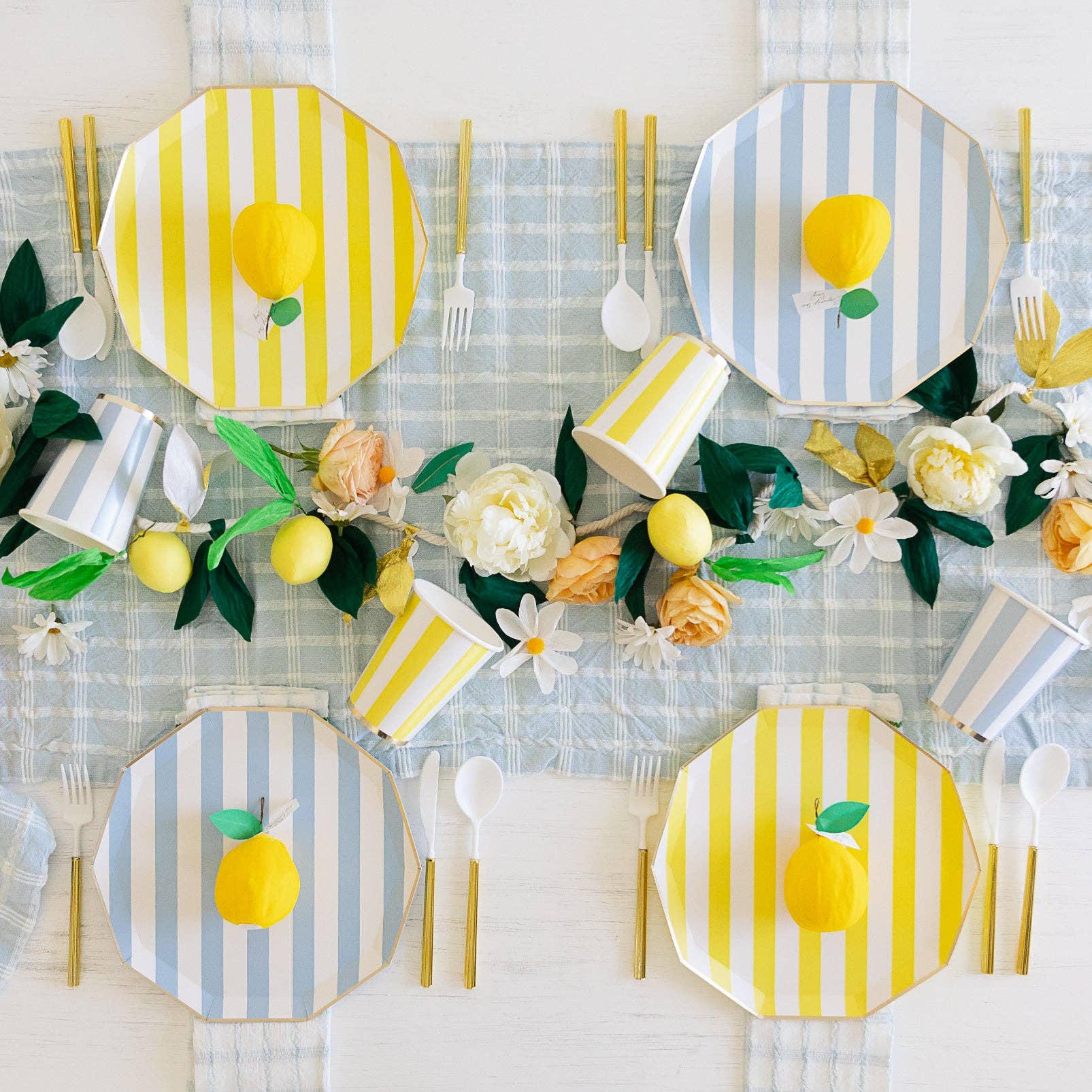 Decorative table setting with lemon-themed plates, cutlery, and flowers on a checkered tablecloth.