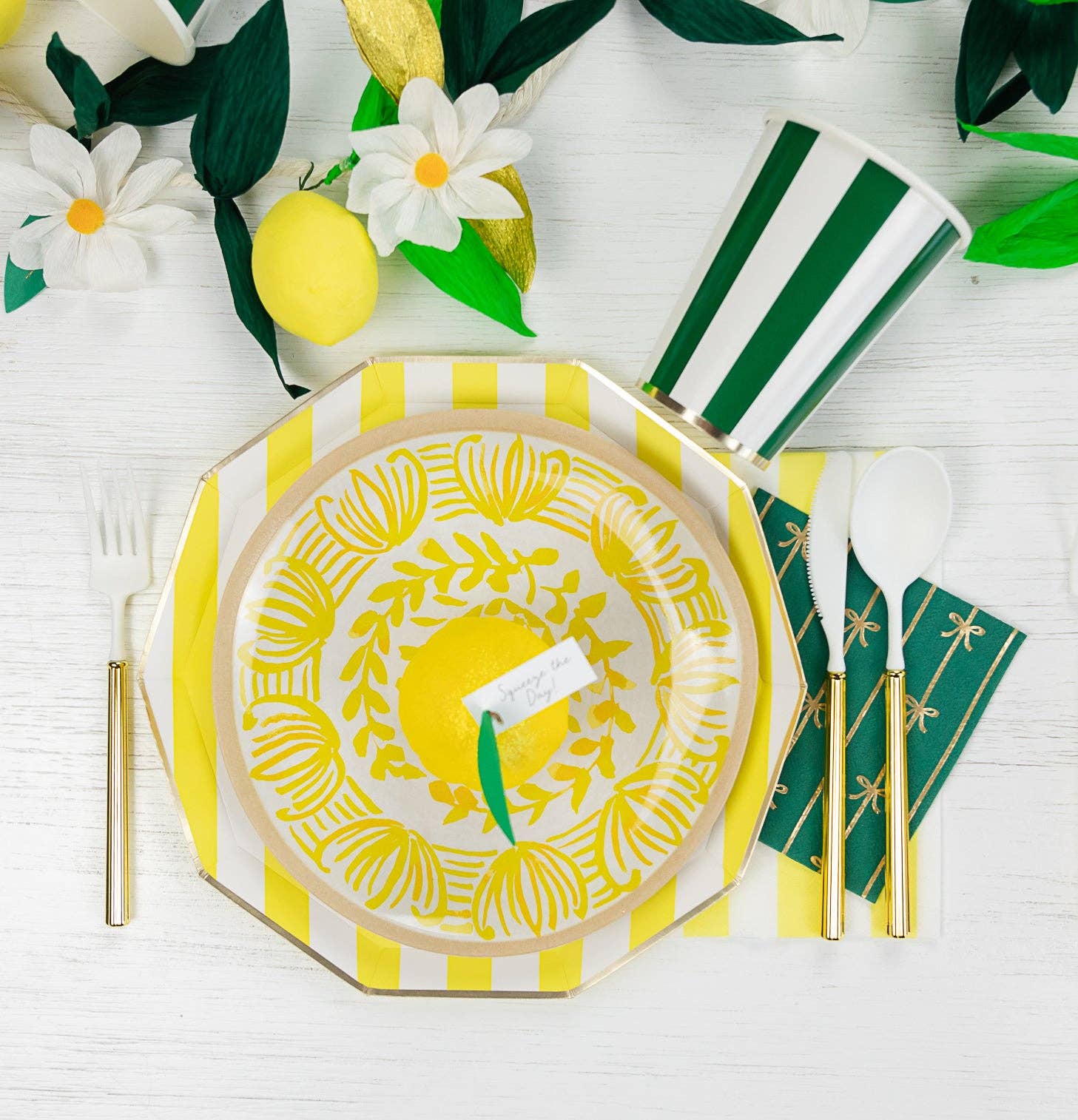 Decorative table setting with yellow and white plate, green and white striped napkin, and floral elements on a white surface.