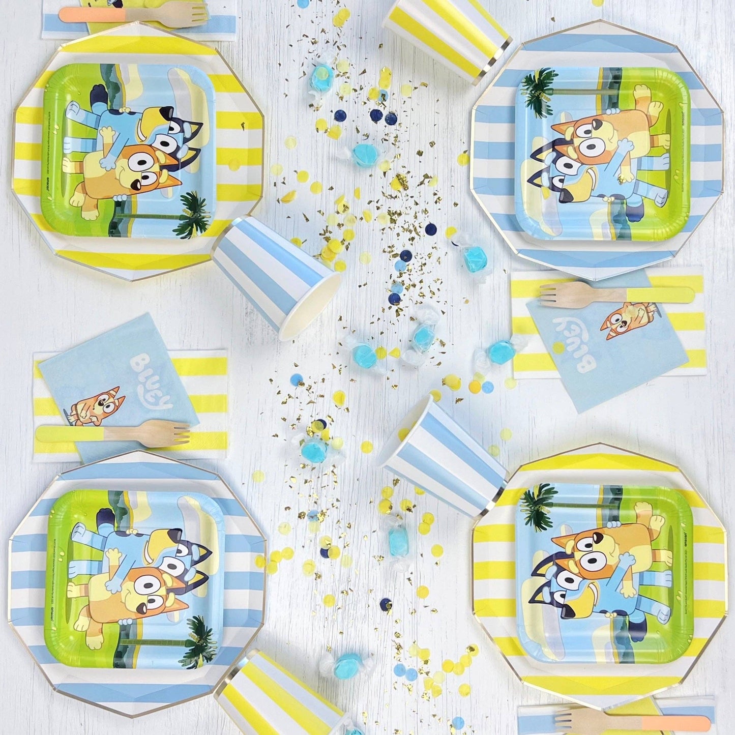 Children's party tableware with cartoon character plates, cups, and napkins on a white surface.