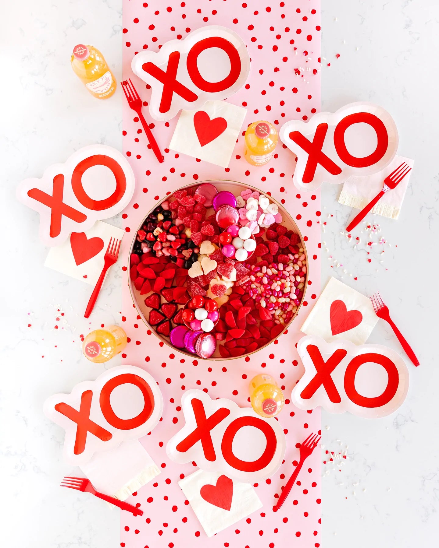 valentine's set up with xo shaped paper plates, heart napkins, candy and confetti
