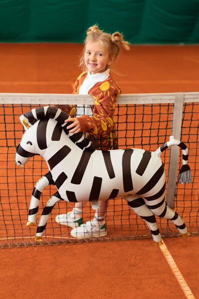 little girl on tennis court playing with air filled zebra foil balloom